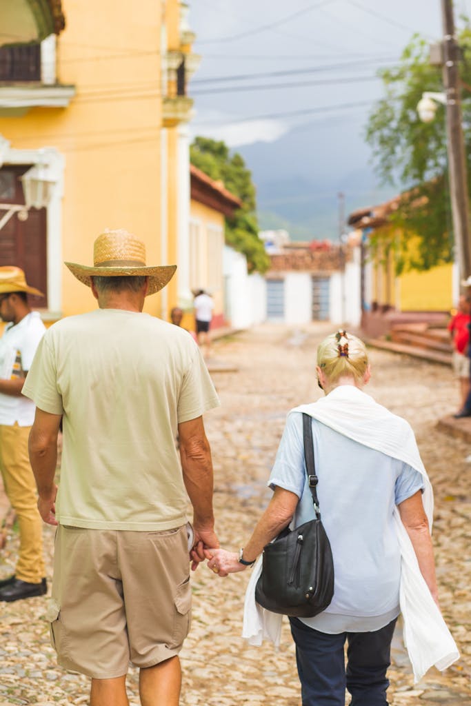 An older couple holding hands and walking down a cobblestone street in a vibrant Cuban town.